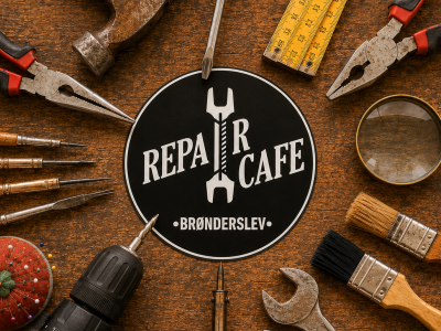 Repair Café Brønderslevs runde logo, omgivet af forskelligt håndværktøj på en slidt træbordplade.
