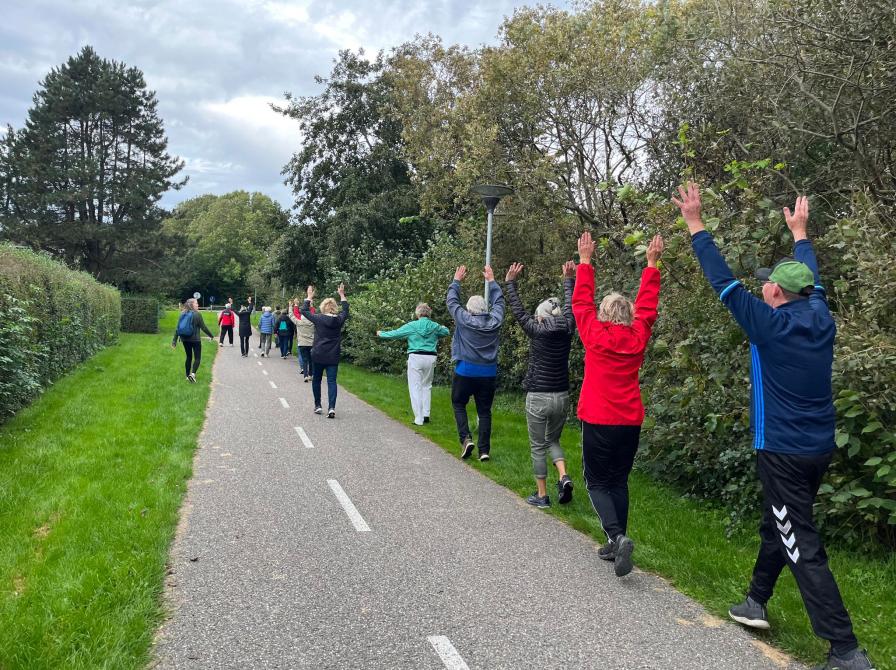 En gruppe mennesker, set bagfra, går i vejsiden med hænderne over hovedet.